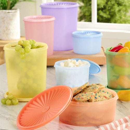 A variety of colorful, round plastic storage containers are shown, each filled with items like grapes, marshmallows, cookies, and sliced vegetables, with lids either on or beside them.