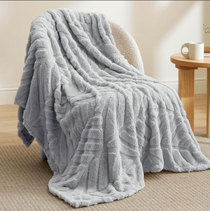 A gray, fluffy blanket with a textured pattern is draped over a chair, next to a wooden side table with a mug on it.