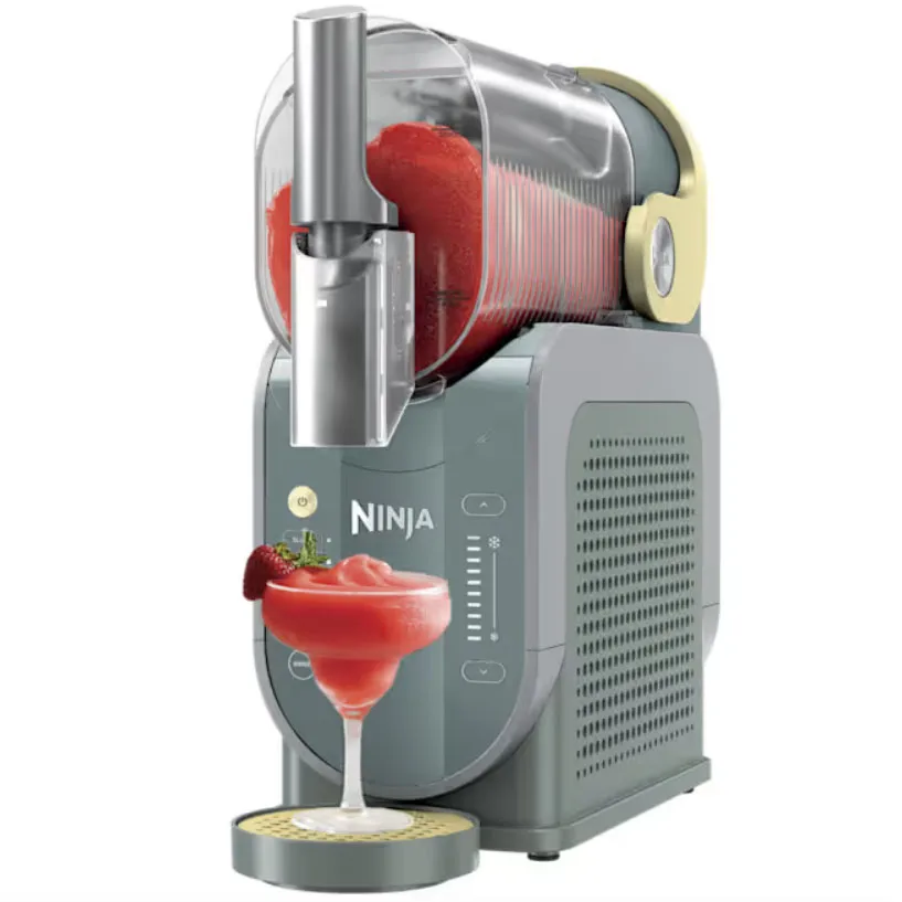 A Ninja drink machine dispenses a strawberry slushy into a martini glass, featuring a transparent container and control panel on the front.