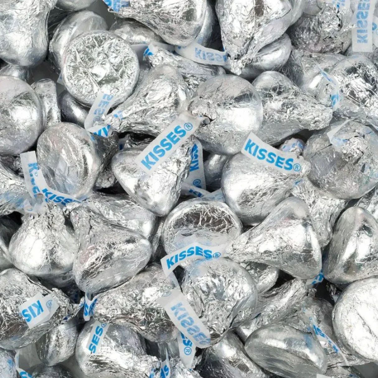 5lbs of Hershey's Kisses, wrapped in silver foil with a distinctive paper plume labeled \“KISSES,\“ scattered in a pile.