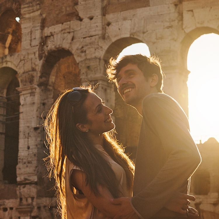 A couple embracing in front of the Colosseum, with the sunlight creating a warm, golden ambiance.
