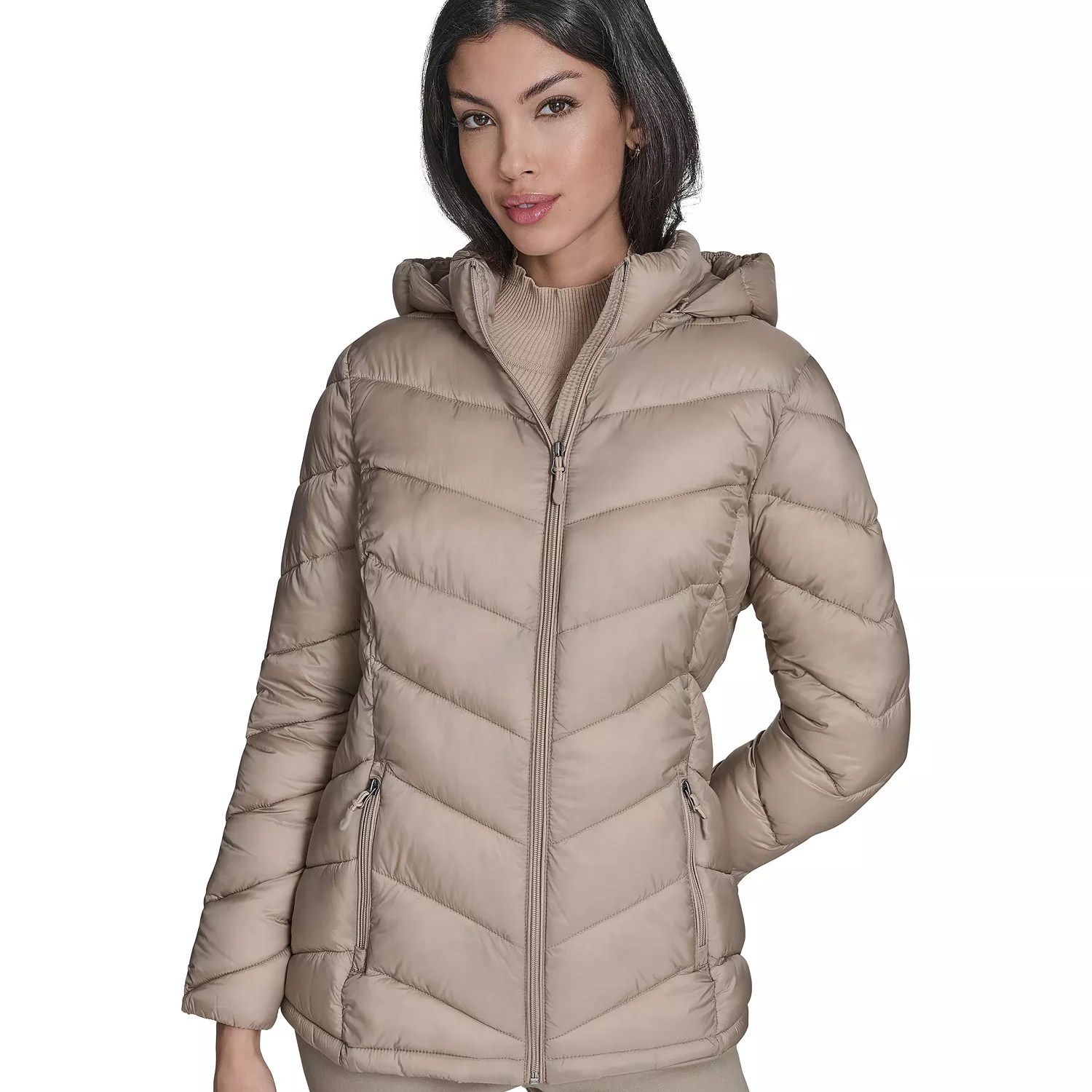 A woman is wearing a beige hooded puffer jacket with a front zipper and two zippered pockets. The jacket features a chevron quilted pattern.