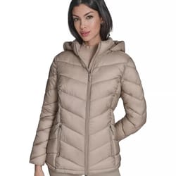 A woman is wearing a beige hooded puffer jacket with a front zipper and two zippered pockets. The jacket features a chevron quilted pattern.
