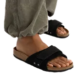 A person wearing green corduroy pants and black open-toe sandals with a cork sole and adjustable strap.