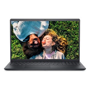 A Dell Inspiron laptop is displayed with a screen showing two people lying on grass, blowing bubblegum. The design is sleek and modern with a dark-colored keyboard and a thin bezel.