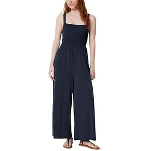 A woman is wearing a navy blue sleeveless jumpsuit with wide legs, paired with flat sandals.