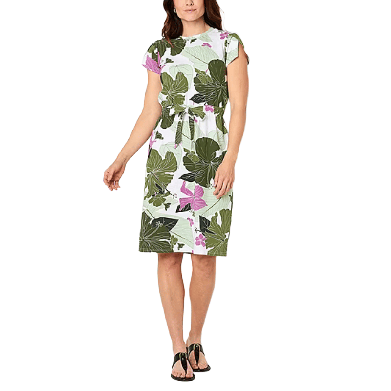 A woman wears a knee-length dress featuring a green and pink leaf pattern, with short sleeves and a waist tie, paired with black sandals.