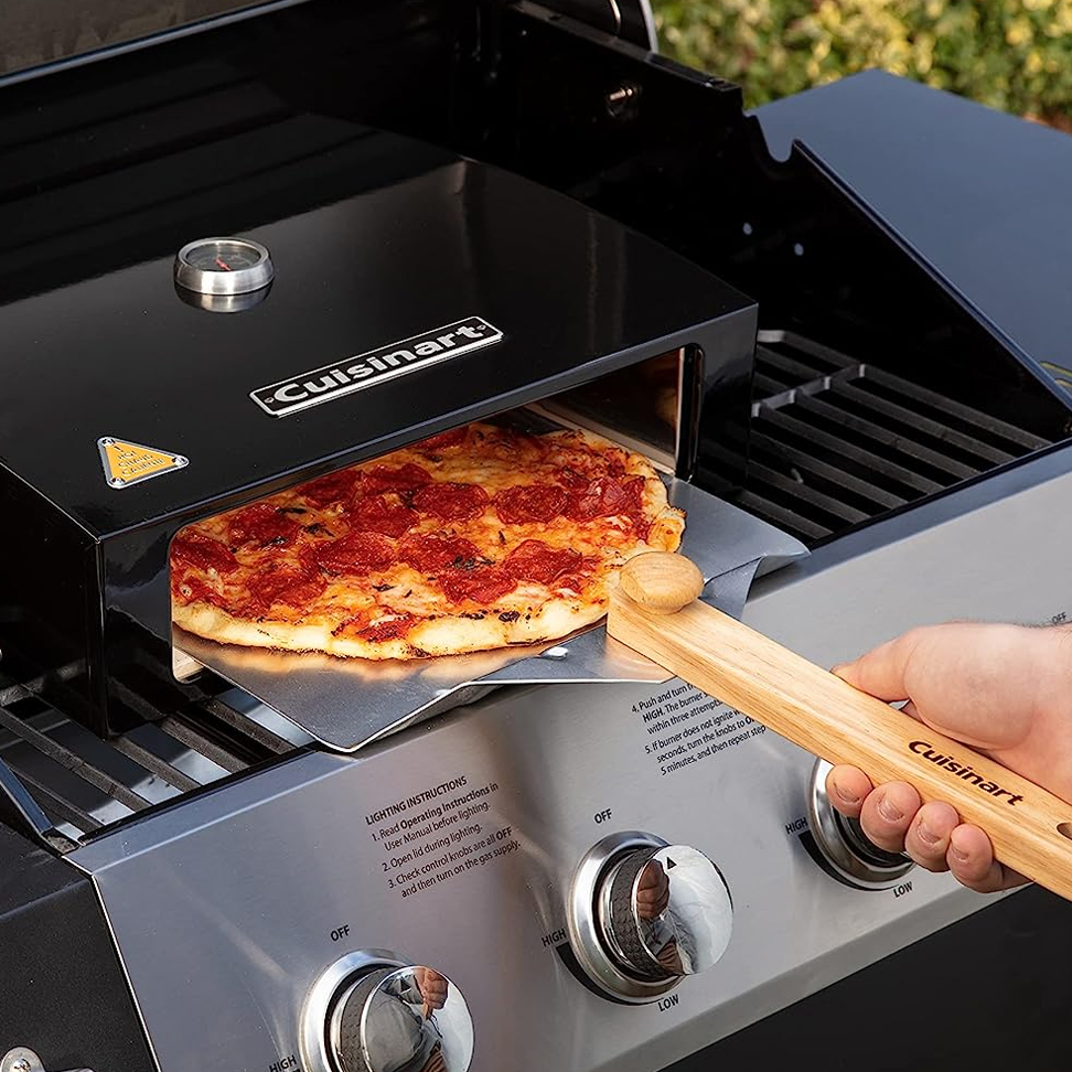 A Cuisinart pizza oven with a pizza being removed using a wooden pizza peel.