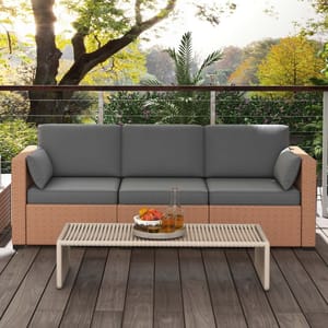 Outdoor rattan sofa with gray cushions and matching coffee table, set on a wooden deck with lush greenery and trees in the background.