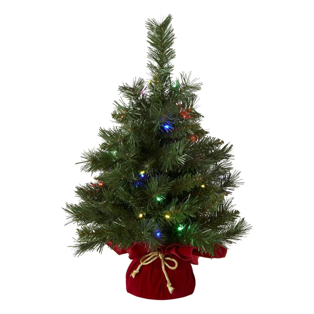 A small artificial Christmas tree decorated with multicolored lights, set in a red base cover tied with a gold ribbon.