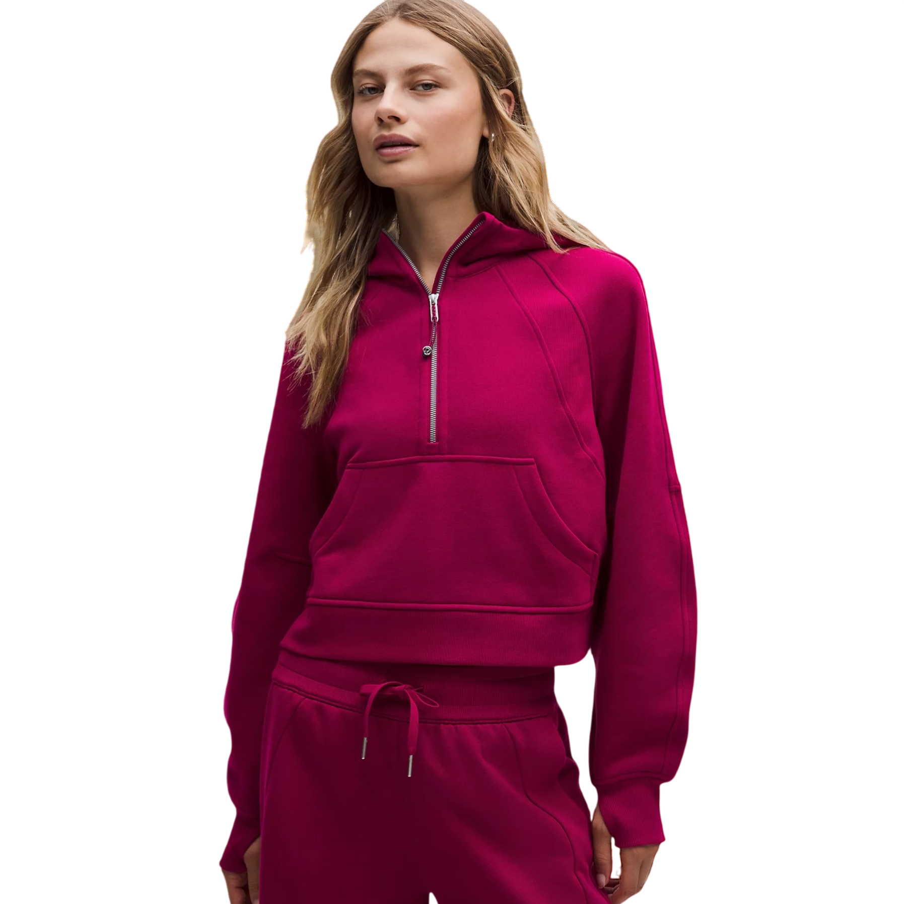 A female model wearing a magenta cropped hoodie with a half-zip and front pocket, paired with matching drawstring sweatpants.