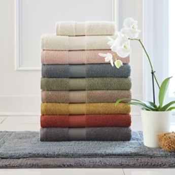 A stack of colorful bath towels, ranging from light to dark shades, alongside a white orchid and a gray bath mat.