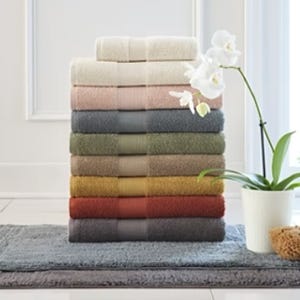 A stack of colorful bath towels, ranging from light to dark shades, alongside a white orchid and a gray bath mat.