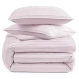 A stack of light pink, pleated bedding items, including two pillows and a folded comforter.