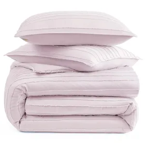 A stack of light pink, pleated bedding items, including two pillows and a folded comforter.
