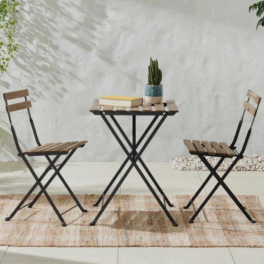 A bistro set with two folding chairs and a small round table with wood slats and metal frames, featuring a potted plant and books on the table.