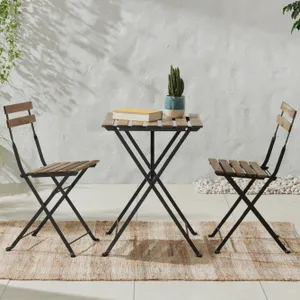 A bistro set with two folding chairs and a small round table with wood slats and metal frames, featuring a potted plant and books on the table.