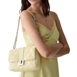 A woman with a yellow quilted handbag on her shoulder, wearing a light yellow lace-trimmed camisole dress and a delicate necklace.