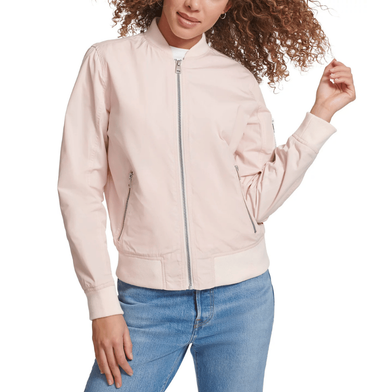 A light pink bomber jacket with a front zipper closure, zippered side pockets, and ribbed cuffs and hem. The jacket features a casual, chic style paired with blue jeans.