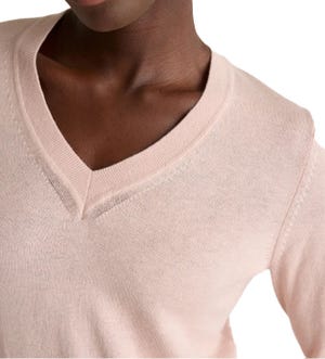 A close-up of a light pink V-neck sweater featuring ribbed detailing at the neckline and stitching accents on the shoulders and sides.
