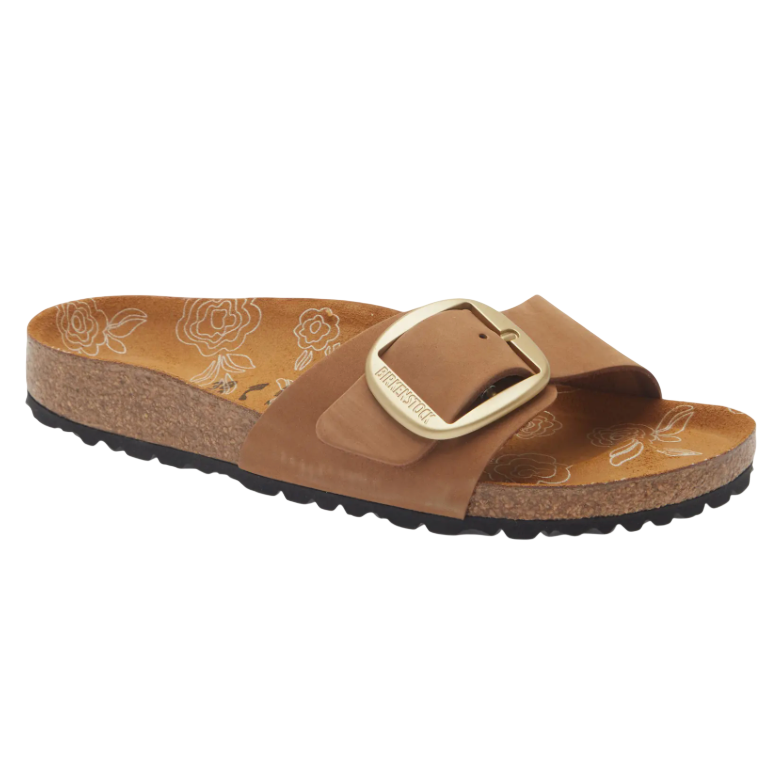 A brown Birkenstock sandal with a large gold buckle and a cork sole. The footbed features a floral pattern.