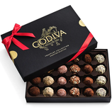 A black box labeled \“Godiva Belgium 1926\“ with a red ribbon contains an assortment of chocolate truffles in various flavors and coatings.