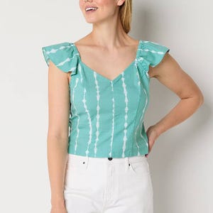 Woman wearing a mint green tie-dye blouse with ruffle sleeves paired with white pants.