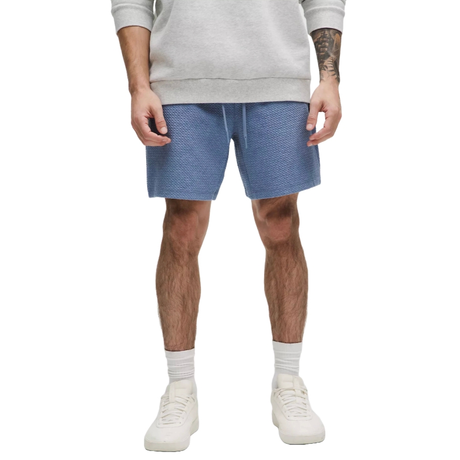 Blue double-knit cotton shorts with a textured pattern and drawstring waist, paired with a light-colored sweatshirt and white sneakers.