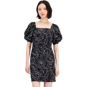 A woman is wearing a black shift dress with puff sleeves and white floral embroidery.
