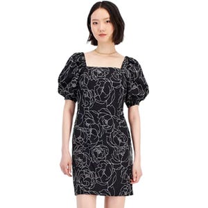 A woman is wearing a black shift dress with puff sleeves and white floral embroidery.
