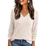 A woman is wearing a light beige ribbed V-neck sweater paired with blue jeans. She's accessorized with a pendant necklace and drop earrings.