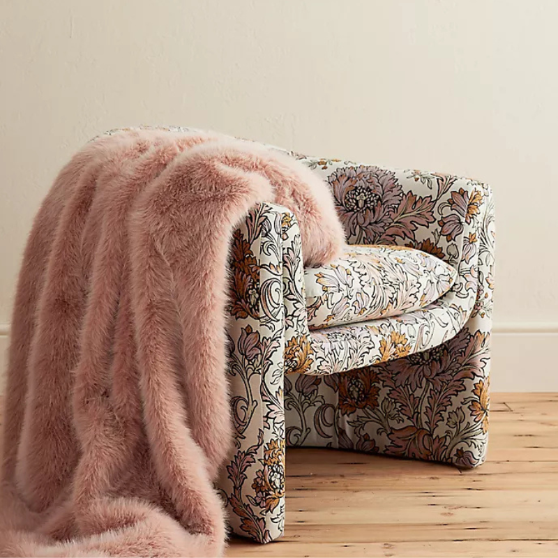 A fluffy, pink faux-fur throw blanket draped over a floral-patterned armchair. The throw adds a cozy and elegant touch to the decor.