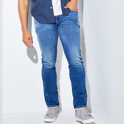 A person wearing blue jeans, a navy-blue shirt with a white underlayer, and grey sneakers.