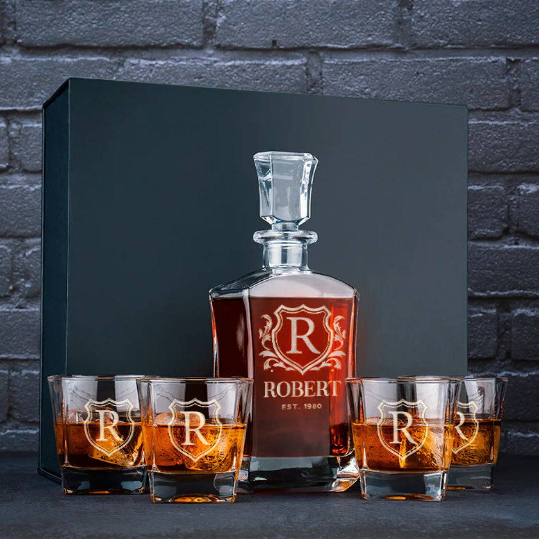 A personalized liquor decanter set includes a decanter and four glasses, each etched with the name \“Robert,\“ an initial \“R,\“ and \“Est. 1980,\“ suggesting a custom or celebratory design.