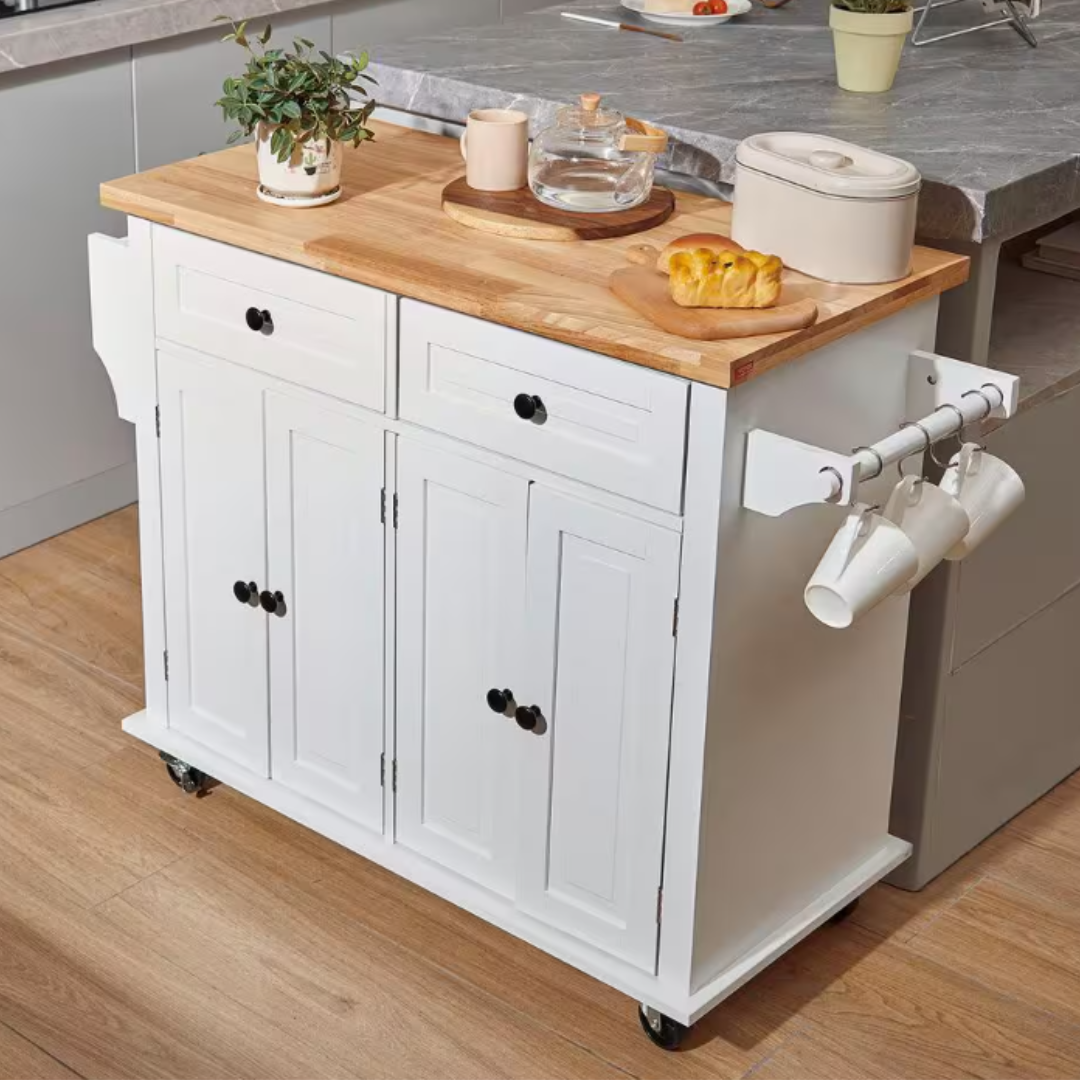 White rolling kitchen island with a wooden countertop, two drawers, and two cabinets, featuring a side rack holding mugs. Includes a potted plant, a jug, a cup, storage container, and a small cutting board with a pastry on top.