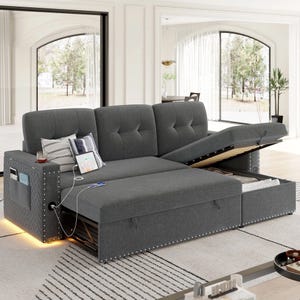 A gray sectional sofa with a pull-out bed and storage compartment. It features stud detailing, built-in lights, and a charging station with pockets for devices and magazines.