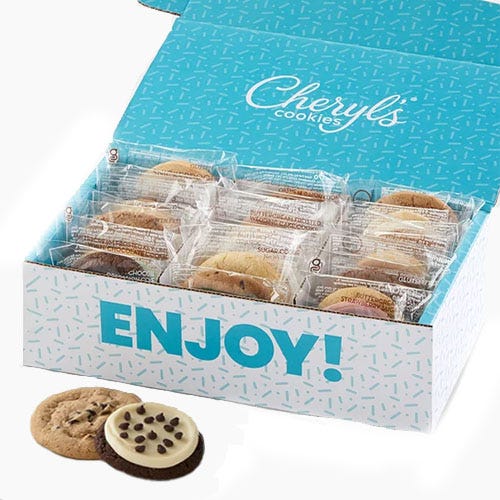 Box of individually wrapped Cheryl's Cookies with a visible \“ENJOY!\“ message on the lid. Two cookies are shown outside, one with chocolate chips and another with icing and chocolate chips.