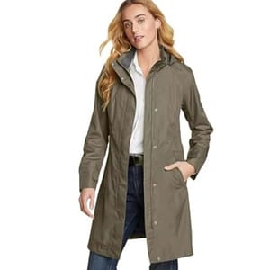 A woman is wearing a long, olive-green trench coat over a white shirt and blue jeans.