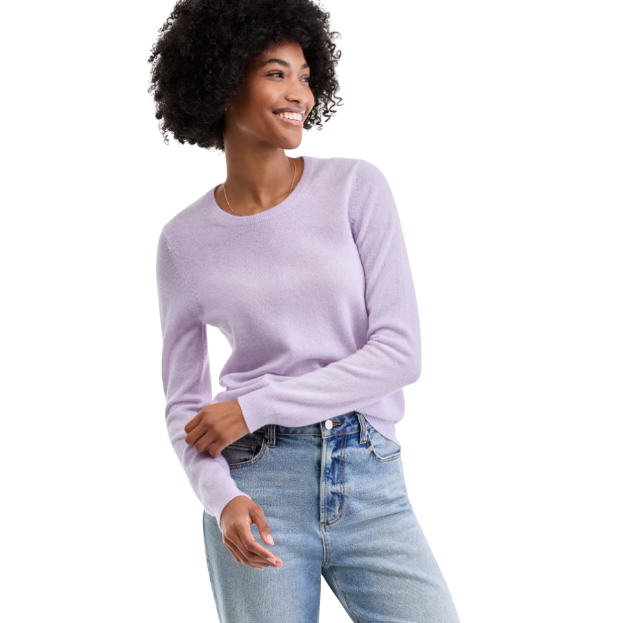 A person wearing a light purple sweater paired with light blue jeans, smiling and looking to the side.