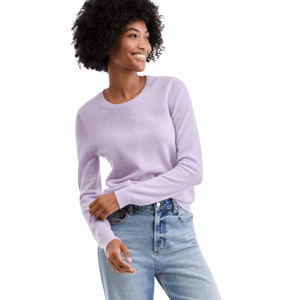 A person wearing a light purple sweater paired with light blue jeans, smiling and looking to the side.