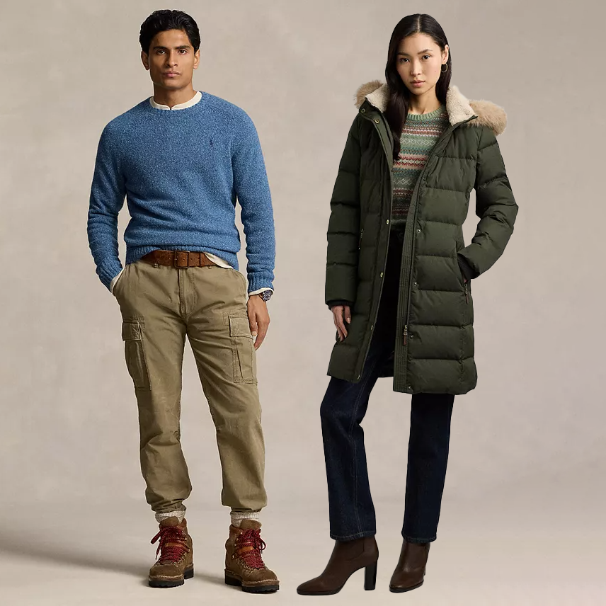 A man is wearing a blue sweater, khaki cargo pants, and brown boots, while a woman is dressed in a green puffer coat with a fur-trimmed hood, patterned sweater, dark jeans, and brown heeled boots.