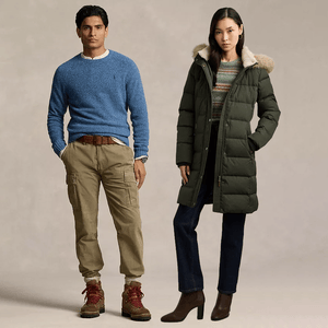 A man is wearing a blue sweater, khaki cargo pants, and brown boots, while a woman is dressed in a green puffer coat with a fur-trimmed hood, patterned sweater, dark jeans, and brown heeled boots.