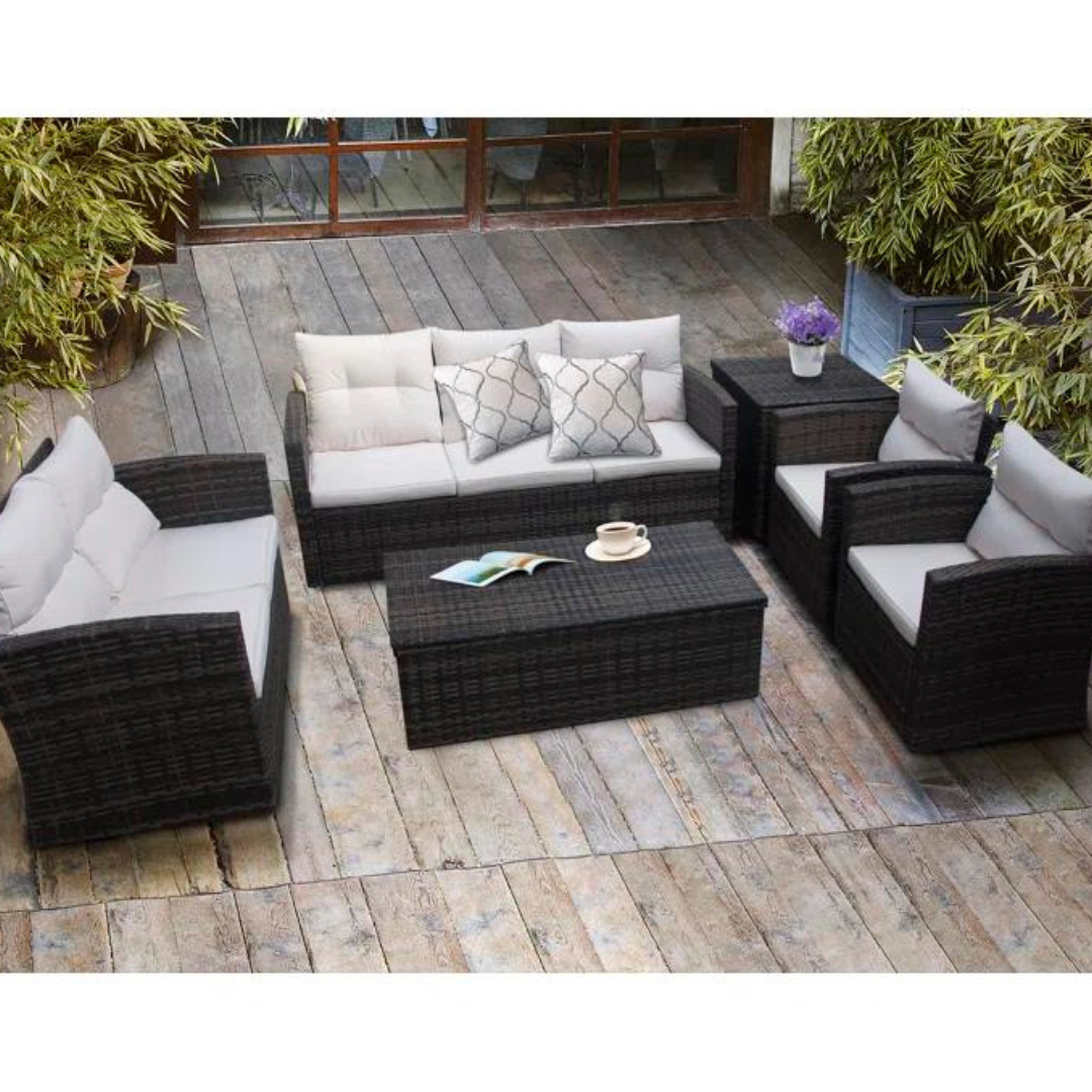A wicker patio furniture set consisting of a sofa, two chairs, and a coffee table, all with white cushions, displayed outdoors.