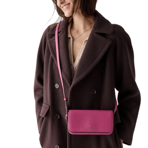 A woman wearing a dark brown coat holds a bright pink crossbody bag.