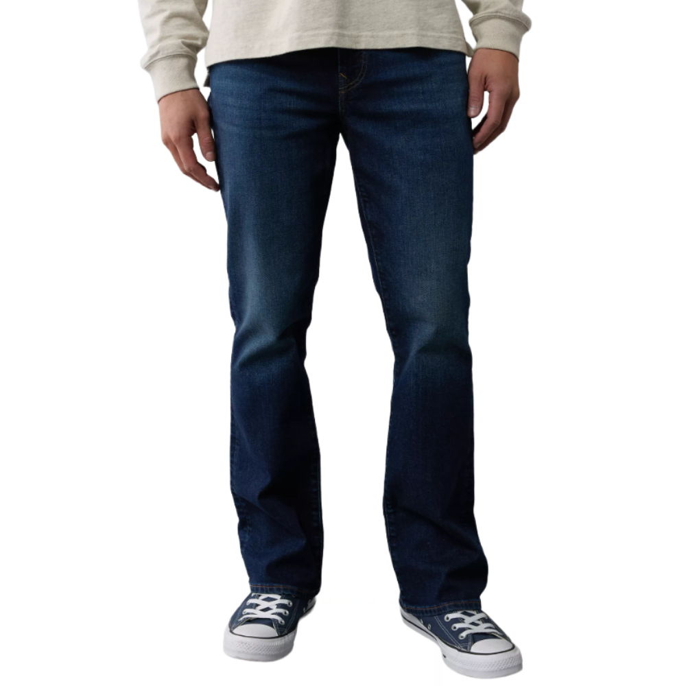 A person wearing dark blue jeans and navy low-top sneakers with white laces, paired with a light-colored long-sleeve shirt.