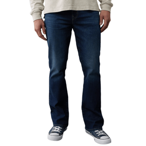 A person wearing dark blue jeans and navy low-top sneakers with white laces, paired with a light-colored long-sleeve shirt.