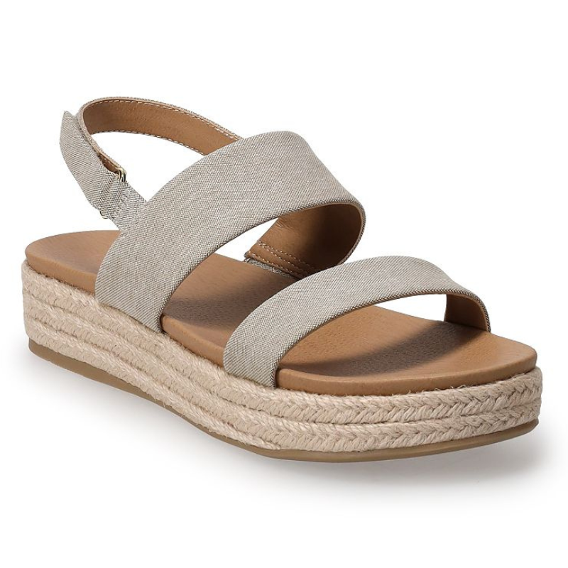 A beige sandal with a thick, woven espadrille-style platform and two wide fabric straps across the foot, featuring a heel strap with buckle closure.