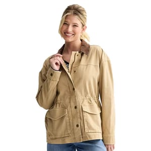 A person wears a light brown jacket with a corduroy collar, button-down front, elastic waistband, and two flap pockets, paired with blue jeans and a striped shirt underneath.