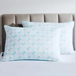 Two rectangular pillows with a repeating pattern of blue anchors are placed on a bed with a taupe upholstered headboard.