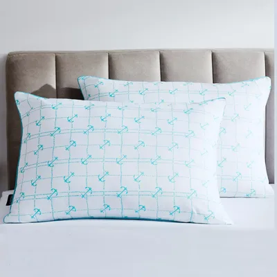 Two rectangular pillows with a repeating pattern of blue anchors are placed on a bed with a taupe upholstered headboard.